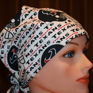 May include: White and black patterned head covering featuring the text "HOUSTON TEXANS" and team logos. The head covering is tied at the back and is designed to be worn on the head.