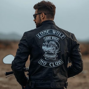 Peut inclure: Une veste en cuir noir avec un grand écusson au dos portant le texte LONE WOLF NO CLUB et une illustration de loup portant des lunettes de protection. La veste a un col montant, des manches longues et une ceinture à la taille, portée avec des lunettes.