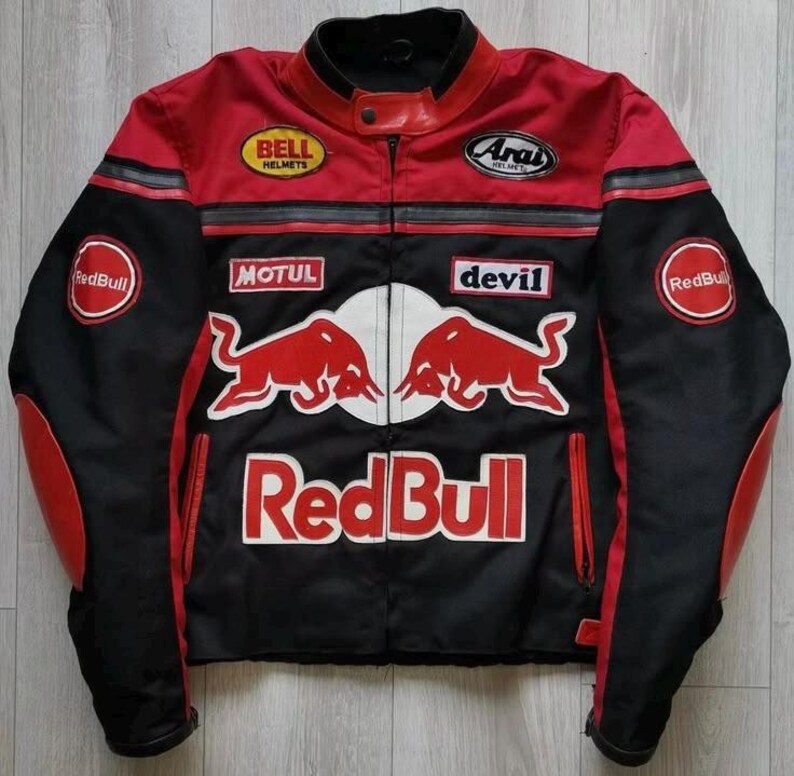 May include: A black and red motorcycle jacket with multiple logos, including "Red Bull," "Bell Helmets," and "Arai." The jacket features a zipper closure, red accents on the shoulders and sleeves, and a stand-up collar.