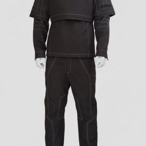 Puede incluir: Traje t&aacute;ctico negro con costuras blancas. El conjunto incluye una parte superior de cuello alto con acolchado en los hombros y un pantal&oacute;n a juego. El traje se muestra en un maniqu&iacute; sobre un fondo liso.