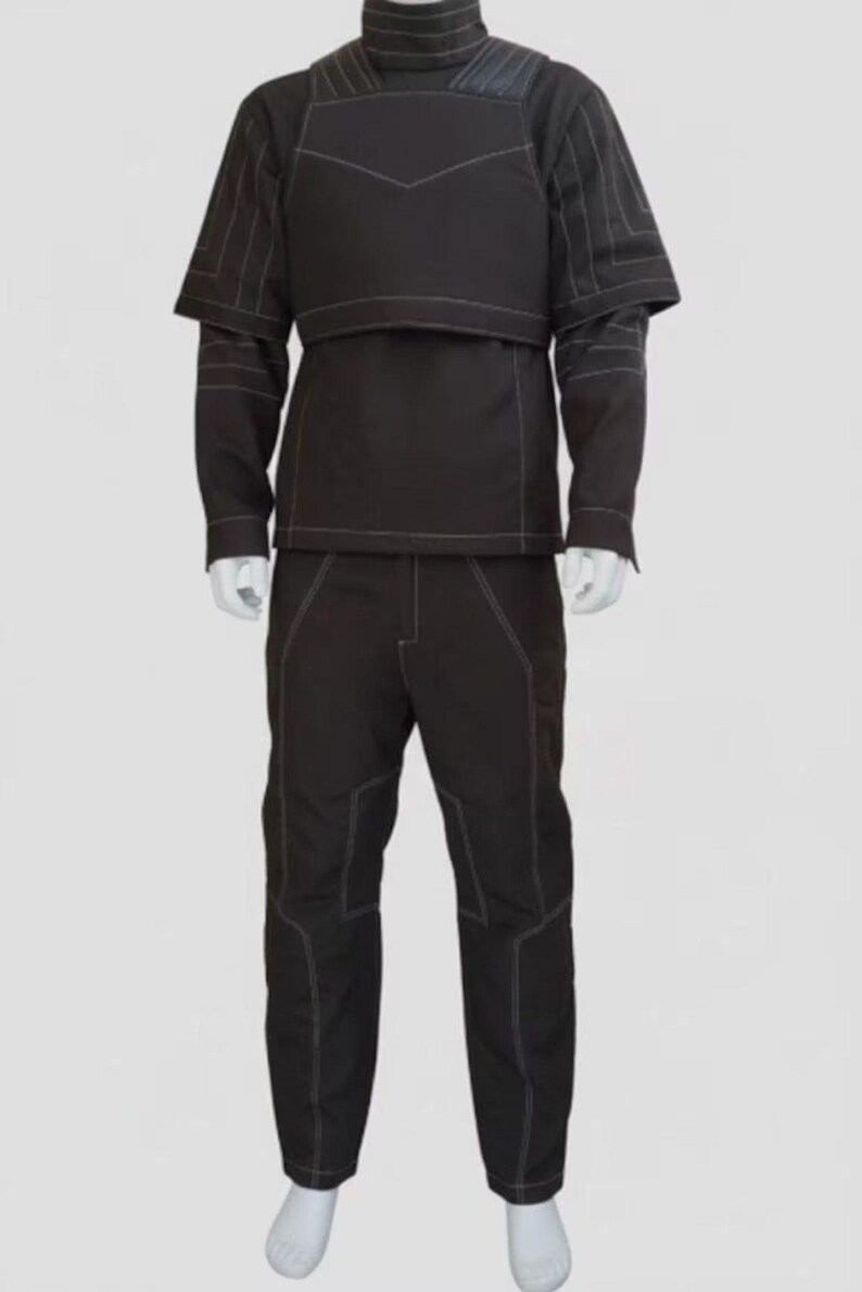 Puede incluir: Traje t&aacute;ctico negro con costuras blancas. El conjunto incluye una parte superior de cuello alto con acolchado en los hombros y un pantal&oacute;n a juego. El traje se muestra en un maniqu&iacute; sobre un fondo liso.