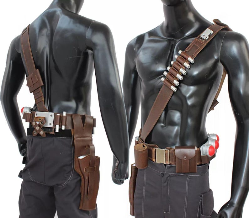 May include: A brown leather utility belt and shoulder strap set with silver accents and multiple pouches. The belt features a holster, a small pouch, and several silver-capped cylinders. The set is displayed on a mannequin.