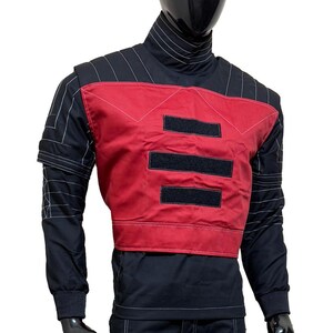 May include: Black and red tactical jacket with white stitching details. The jacket features a high collar, long sleeves, and a red panel on the chest with three black velcro patches. The jacket is displayed on a mannequin.