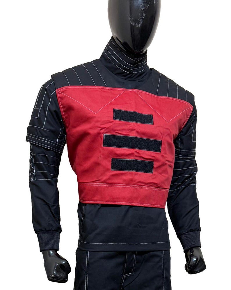 May include: Black and red tactical jacket with white stitching details. The jacket features a high collar, long sleeves, and a red panel on the chest with three black velcro patches. The jacket is displayed on a mannequin.