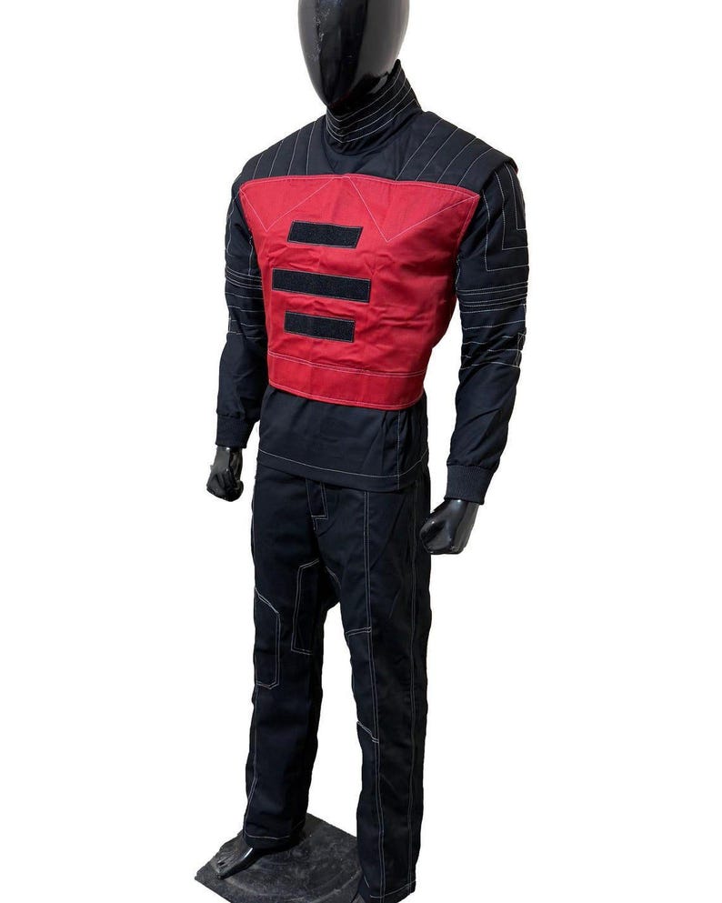 May include: Black and red jumpsuit with white stitching. The outfit includes a high-neck top, a red vest with three black horizontal stripes, and matching pants. The mannequin is standing on a dark gray base.