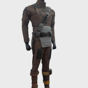 Puede incluir: Un disfraz marr&oacute;n y gris con cuello alto, mangas largas y pantalones a juego. El atuendo incluye una placa pectoral gris, un cintur&oacute;n negro y una bandolera con bolsillos. Guantes negros y botas marrones completan el conjunto.