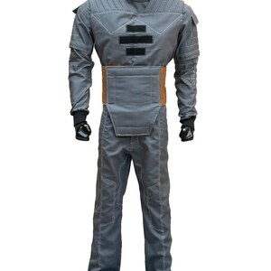 May include: A gray jumpsuit with white stitching, a high collar, and a brown belt. The costume has padded sections on the chest and shoulders, with black gloves and a black head covering. The outfit is displayed on a mannequin.