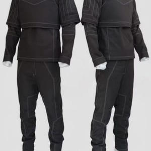 Puede incluir: Dos trajes t&aacute;cticos negros. Cada atuendo incluye una chaqueta de cuello alto con panel en el pecho y mangas cortas, una camiseta de manga larga y pantalones a juego. Las costuras blancas acent&uacute;an las costuras. Los trajes se exhiben en maniqu&iacute;es.