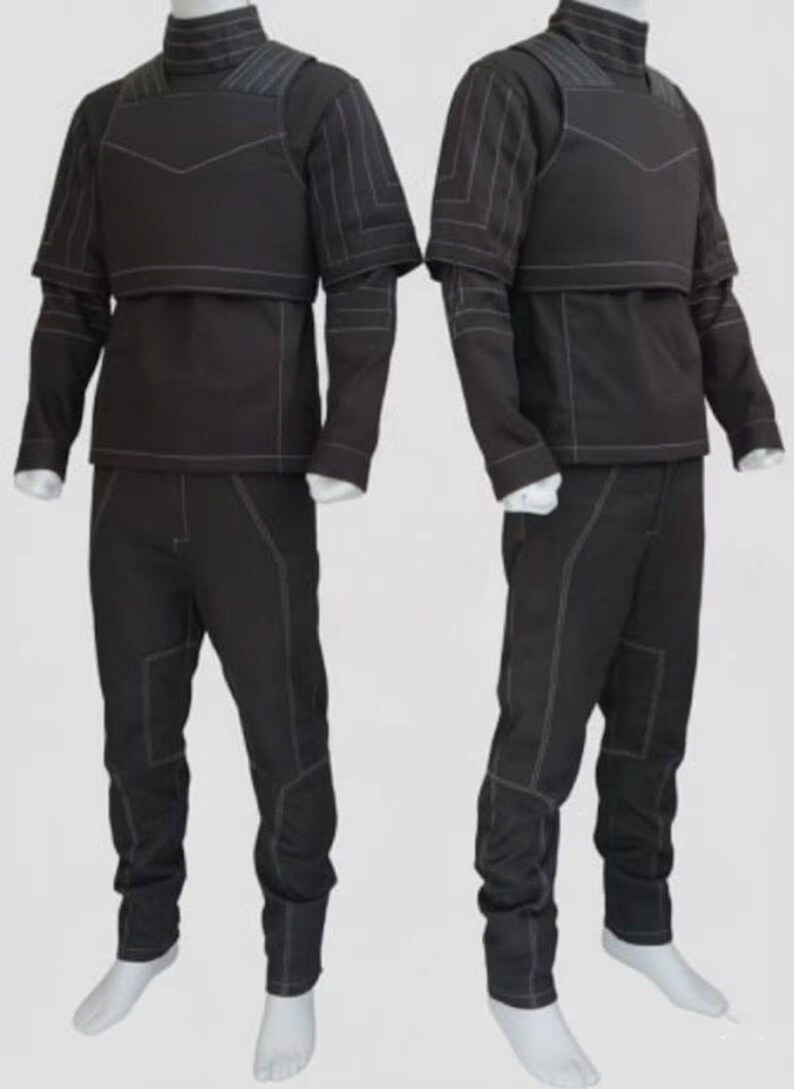 Puede incluir: Dos trajes t&aacute;cticos negros. Cada atuendo incluye una chaqueta de cuello alto con panel en el pecho y mangas cortas, una camiseta de manga larga y pantalones a juego. Las costuras blancas acent&uacute;an las costuras. Los trajes se exhiben en maniqu&iacute;es.