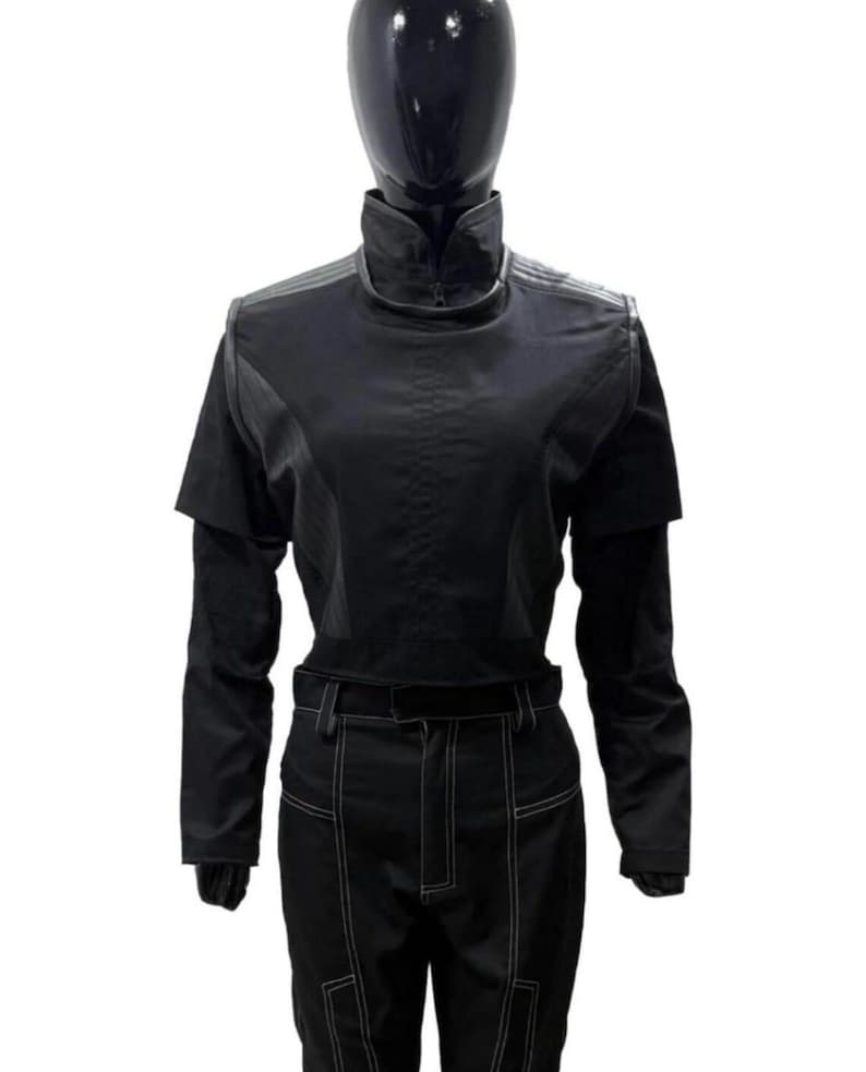 Puede incluir: Mono negro con cuello alto y mangas largas. El atuendo presenta un corpi&ntilde;o ajustado, mangas cortas sobre mangas largas y pantalones con detalles de costura blancos. El maniqu&iacute; lleva un casco negro.