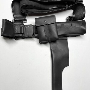 Puede incluir: Un cintur&oacute;n utilitario de cuero negro con m&uacute;ltiples bolsas y una funda. El cintur&oacute;n tiene presillas para sujetar municiones y un cierre de hebilla. El dise&ntilde;o est&aacute; detallado con costuras y remaches.