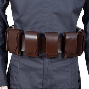 May include: A brown leather belt with five attached pouches. The belt is worn over a dark blue uniform. The pouches are rectangular with a flap closure. The belt and pouches appear to be made of a smooth leather material.