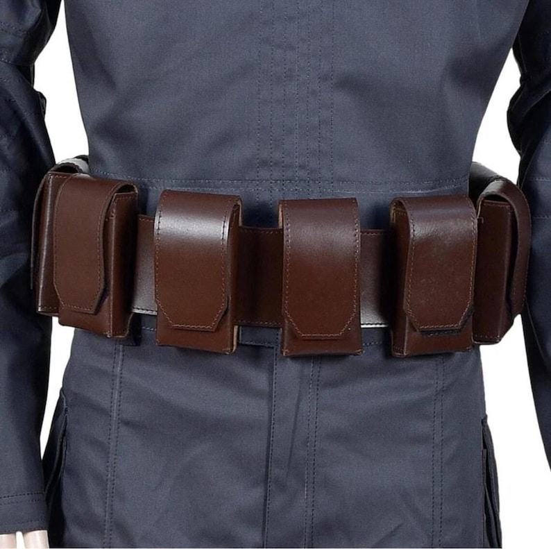 May include: A brown leather belt with five attached pouches. The belt is worn over a dark blue uniform. The pouches are rectangular with a flap closure. The belt and pouches appear to be made of a smooth leather material.