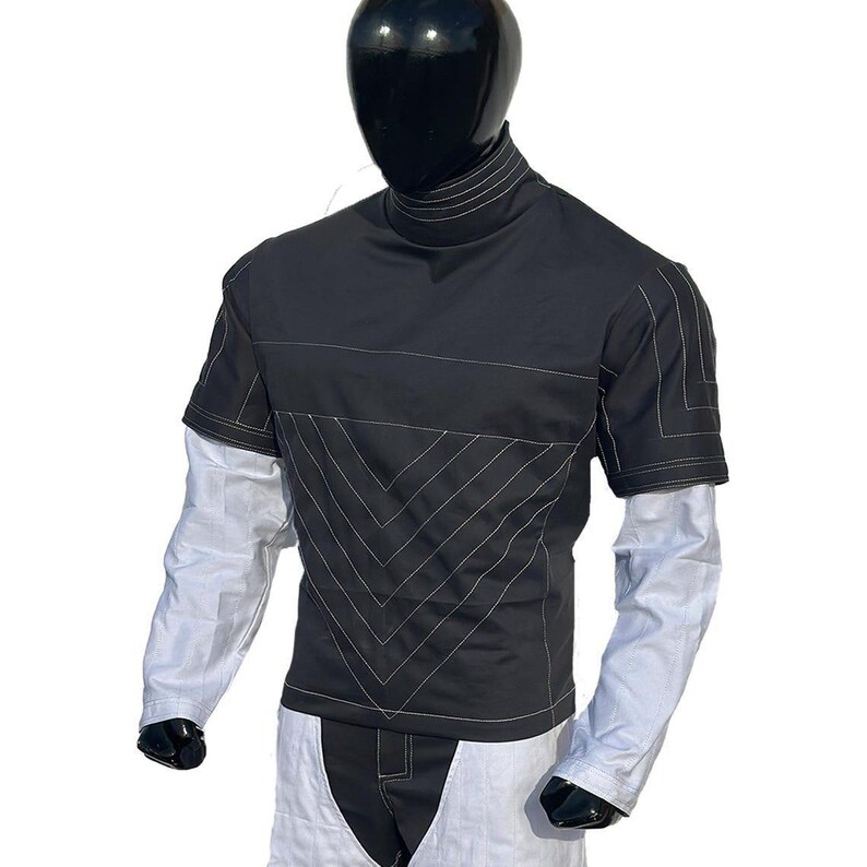 May include: Black short-sleeve shirt with white stitching details and a high collar. The shirt has a geometric design on the front and is layered over a white long-sleeve shirt. The mannequin is wearing white pants.