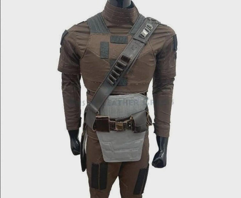 Puede incluir: Traje t&aacute;ctico marr&oacute;n con peto, bandolera y cintur&oacute;n. El atuendo incluye una camisa de manga larga, pantalones y guantes. El disfraz tiene m&uacute;ltiples bolsillos y un protector gris para la parte inferior del torso.