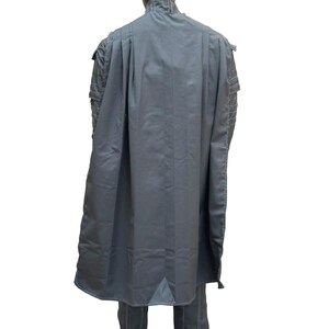 May include: A gray costume with a cape, displayed on a mannequin. The outfit includes a long cape, a high-collared jacket, and matching pants. White stitching accents the seams of the jacket and pants. The mannequin has a black head.