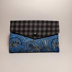May include: A rectangular envelope-style clutch featuring a black and gray gingham check pattern on the top flap and a vibrant blue fabric with a detailed black and gold paisley print on the main body, secured with a single black snap button.