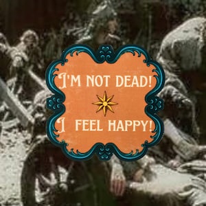 May include: A rectangular sticker with rounded, ornate edges featuring an orange background and a dark teal border. The text "I'M NOT DEAD! I FEEL HAPPY!" is printed in white, with a yellow eight-pointed star symbol centred between the two lines.