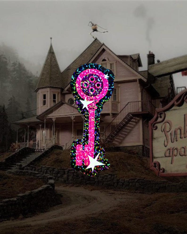 May include: A pink key-shaped decoration with a glittery, multi-colored outline and white star accents. The key is set against a backdrop of a pink house with a dark, overcast sky and a sign that reads "Pink apa".