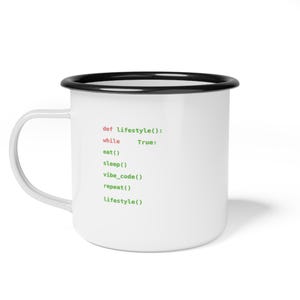 Puede incluir: Taza de esmalte blanco con borde y asa negros. La taza presenta un fragmento de código de programación en texto verde y rojo: "def lifestyle(): while True: eat() sleep() vibe_code() repeat() lifestyle()".