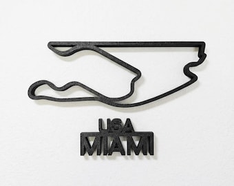 May include: A black 3D-printed wall decoration featuring the outline of the Miami International Autodrome race track. Below the track layout, the text USA MIAMI is displayed in bold, block capital letters, matching the black color.