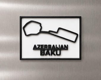 Può includere: Una targa rettangolare da parete con il profilo nero stampato in 3D del circuito cittadino di Baku in Azerbaigian. La mappa del tracciato e la scritta nera AZERBAIJAN BAKU sono montate su uno sfondo rettangolare bianco con cornice nera.