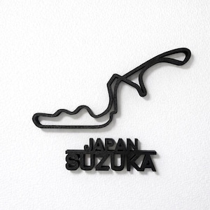 May include: A black, three-dimensional wall-mounted sculpture depicting the Suzuka International Racing Course track layout. Below the track outline, the words JAPAN and SUZUKA are displayed in bold, black, capital sans-serif lettering.