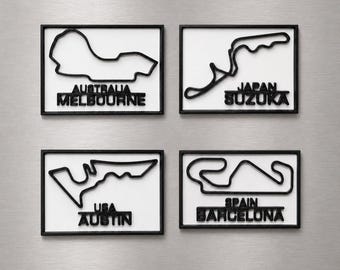 Può includere: Quattro magneti rettangolari con contorni neri in rilievo di circuiti di Formula 1 su sfondo bianco. I circuiti sono etichettati Australia Melbourne, Japan Suzuka, USA Austin e Spain Barcelona con scritte nere in rilievo.