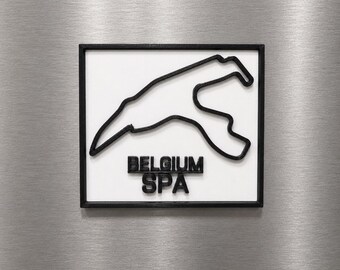 Può includere: Una targa da parete quadrata che presenta un contorno nero in rilievo del circuito di Spa-Francorchamps su sfondo bianco. Il testo BELGIUM SPA è impresso in lettere maiuscole nere sotto il tracciato, il tutto racchiuso in una cornice nera.