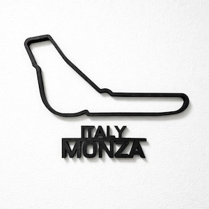 May include: A black wall-mounted sculpture depicting the outline of the Monza race track in Italy. Below the track layout, the words ITALY and MONZA are displayed in bold, black, capital letters, creating a cohesive and dimensional display.