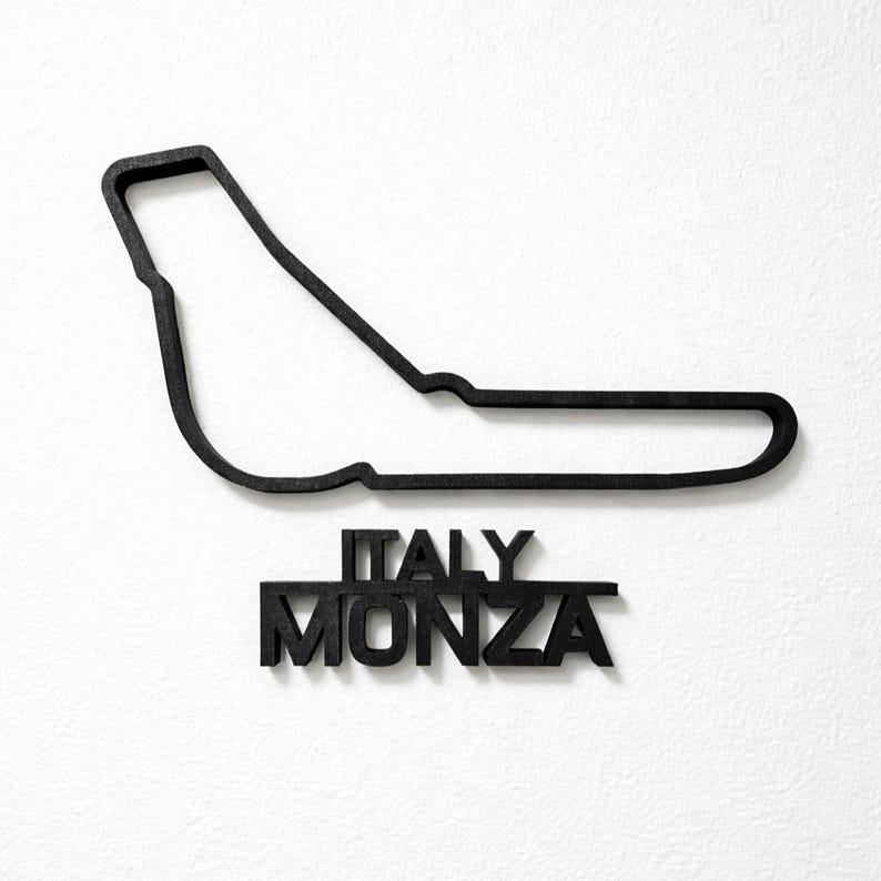 May include: A black wall-mounted sculpture depicting the outline of the Monza race track in Italy. Below the track layout, the words ITALY and MONZA are displayed in bold, black, capital letters, creating a cohesive and dimensional display.