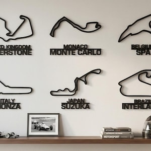Puede incluir: Arte mural negro con contornos de circuitos de carreras famosos, como Silverstone, Mónaco y Spa. Debajo de cada circuito está el nombre del lugar. Una estantería exhibe un coche de carreras de juguete, una foto enmarcada, libros y un casco.
