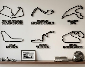 May include: Six black wall-mounted metal outlines of Formula 1 race tracks including Silverstone, Monte Carlo, Spa, Monza, Suzuka, and Interlagos. Each track is labeled with its country and name in bold black lettering below the circuit shape.