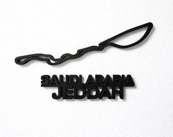 Può includere: Decorazione murale nera raffigurante il tracciato di un circuito e la scritta "SAUDI ARABIA JEDDAH". Il tracciato è una linea continua, e il testo è in grassetto, senza grazie.