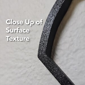 May include: A black, angular object with a rough, granular, and textured surface. The text 'Close Up of Surface Texture' is printed in white on the left side of the image, providing a clear view of the material's finish and physical detail.