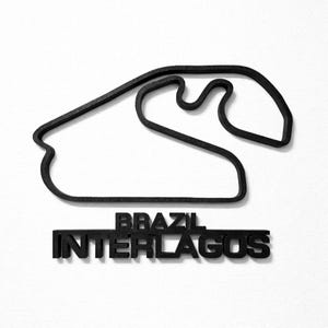May include: A black 3D-printed wall art piece depicting the Interlagos race track layout in Brazil. The object features a continuous black outline of the circuit path positioned above the text BRAZIL INTERLAGOS in bold, block capital letters.