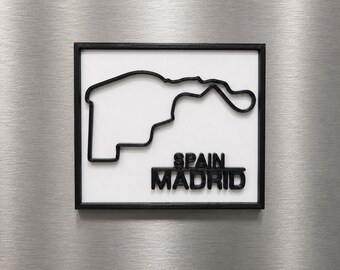 Può includere: Un oggetto da parete quadrato che presenta il contorno nero in rilievo del circuito di gara di Madrid, Spagna, su uno sfondo bianco, racchiuso in una sottile cornice nera. Il testo SPAIN MADRID è visualizzato in lettere nere in rilievo in basso a destra.
