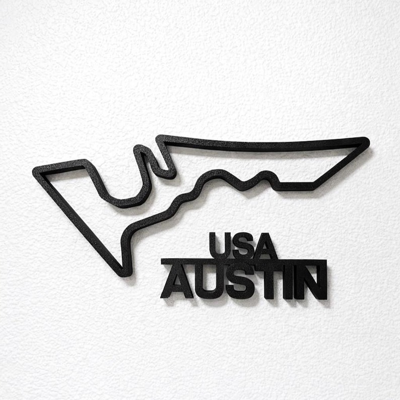 May include: A black wall-mounted sign featuring the outline of the Circuit of the Americas race track in Austin, Texas. Below the track outline, the text USA AUSTIN is displayed in bold, black, capital letters with a textured finish.