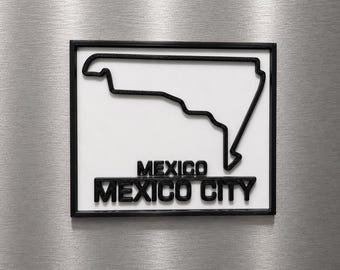 Può includere: Una targa da parete quadrata con cornice nera e sfondo bianco. Presenta un contorno nero in rilievo di una regione geografica sopra il testo nero "MEXICO" e "MEXICO CITY" in un carattere sans-serif in grassetto, creando un alto contrasto.