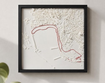 Può includere: Un'opera d'arte da parete quadrata con cornice nera che presenta una mappa in rilievo tridimensionale bianca di una città costiera. Una sottile linea rossa traccia un percorso specifico lungo la costa e attraverso la rete stradale urbana.