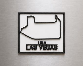 Può includere: Un oggetto da parete quadrato con cornice nera e sfondo bianco. Il contorno nero del circuito di Las Vegas è centrato, con il testo nero USA LAS VEGAS posizionato direttamente sotto il design del tracciato del circuito.