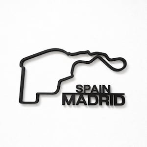 May include: A black wall-mounted sculpture depicting the layout of the Madrid Formula 1 race track. The design features a continuous outline of the circuit with the text SPAIN MADRID positioned in bold, capital letters underneath the track shape.