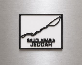 Può includere: Una targa da parete rettangolare con un contorno nero in rilievo del circuito di Jeddah Corniche in Arabia Saudita su sfondo bianco. Il testo SAUDI ARABIA JEDDAH è visualizzato in lettere nere in rilievo sotto il tracciato del circuito.