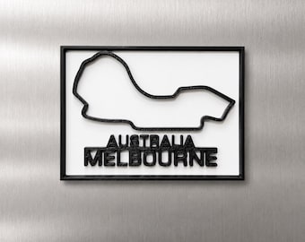 Può includere: Un oggetto da parete rettangolare che presenta il profilo nero in rilievo del circuito di Melbourne in Australia. Il testo nero sotto il tracciato recita AUSTRALIA MELBOURNE. Il design è posto su uno sfondo bianco all'interno di una cornice nera.