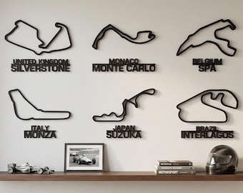 Può includere: Sei profili neri di circuiti di Formula 1 montati a parete, tra cui Silverstone, Monte Carlo, Spa, Monza, Suzuka e Interlagos. Sotto i circuiti, una mensola sostiene una piccola foto incorniciata di un'auto da corsa, tre libri e un casco.
