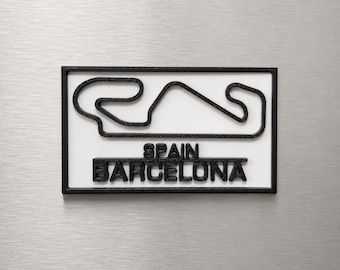 Può includere: Una targa rettangolare da parete con il contorno nero in rilievo del circuito di gara di Barcellona, Spagna, su sfondo bianco. Il testo SPAIN BARCELONA è impresso in lettere nere sotto il tracciato all'interno di una cornice nera.