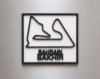 Può includere: Un quadro da parete quadrato con il profilo nero stampato in 3D del circuito di Formula 1 di Bahrain Sakhir su sfondo bianco, racchiuso in una cornice nera. Il testo BAHRAIN SAKHIR è riportato in lettere nere in rilievo sotto il tracciato.