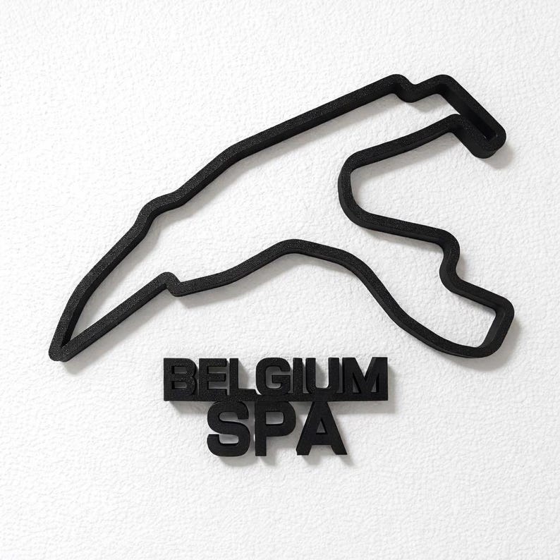 May include: A black, three-dimensional wall-mounted sculpture depicting the layout of the Spa-Francorchamps racetrack in Belgium. Below the track outline, the words BELGIUM and SPA are displayed in bold, black, block-style capital letters.