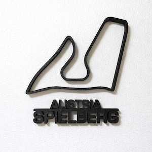 May include: A black 3D-printed wall decoration featuring the outline of the Red Bull Ring racetrack in Spielberg, Austria. Below the track outline, the text AUSTRIA and SPIELBERG are displayed in bold, block capital letters in a matching black finish.
