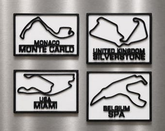Può includere: Quattro magneti rettangolari con contorni neri in rilievo di circuiti di Formula 1 su sfondo bianco. I circuiti sono etichettati come Monaco Monte Carlo, United Kingdom Silverstone, USA Miami e Belgium Spa in lettere nere in rilievo.